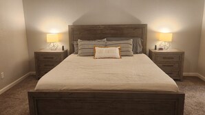 A bedroom with a wooden bed, two bedside tables with lamps, and a pillow with the text "STAY AWAY".