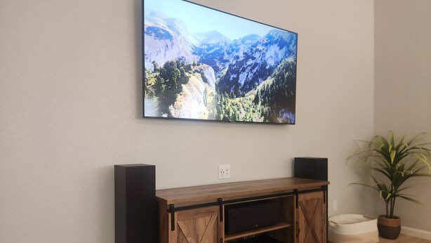 A living room with a mounted flat-screen TV, wooden entertainment center, and a potted plant.