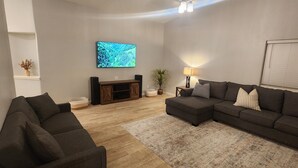 A living room with a sectional sofa, a flat-screen TV, a wooden entertainment unit, and a floor lamp.
