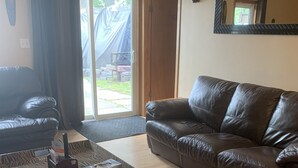 Ein Wohnzimmer mit einer Ledersofa, einem Couchtisch mit Tablett und einer Glastür, die zu einem Außenbereich führt.