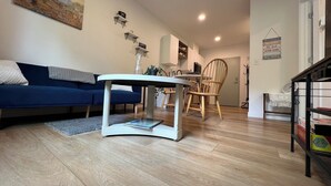 Ein modernes Wohnzimmer mit einem blauen Sofa, einem weißen Couchtisch und einem Essbereich mit einem Holzstuhl.