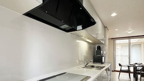 A modern kitchen with a built-in stove, a black range hood, and a dining area with a table and chairs. - Eight Valley Nakamachi (Hiroshima)