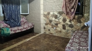 Ein Zimmer mit einer Couch, einem Fenster mit Vorhang, einer Steinwand und einem Fliesenboden.