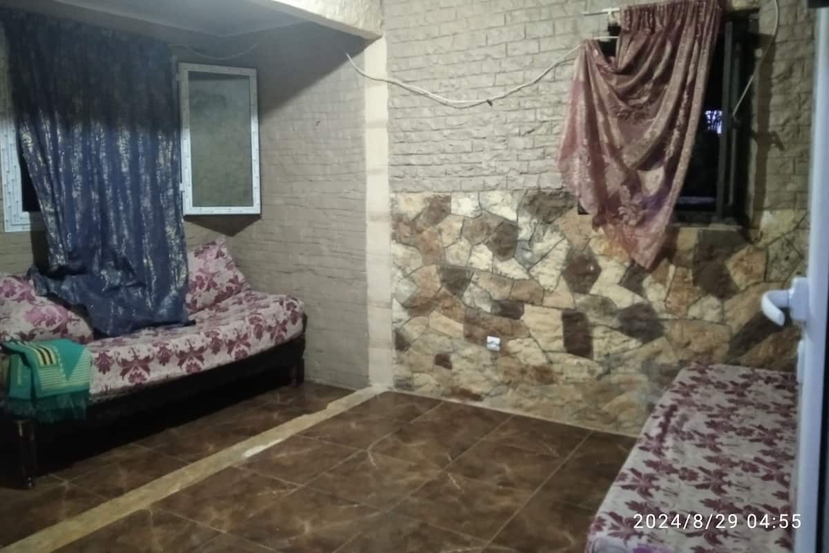 A room with a sofa, a window with a curtain, a stone wall, and a tiled floor.