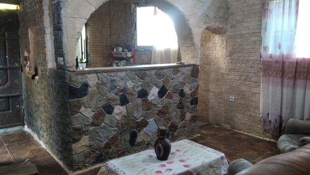 Ein Kamin aus Stein mit rustikalem Bogen, ein Tisch mit blumigem Tischläufer und eine Couch in einem gemütlichen Raum mit Backsteinwänden.