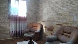 Ein Zimmer mit Backsteinwand, zwei Ledersesseln, einem Tisch mit einer Vase und einem Fenster mit Vorhängen.