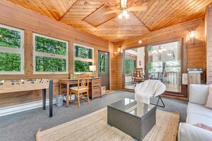 Un intérieur en bois comprenant un canapé, une table à plateau en verre, un bureau en bois et une fenêtre donnant sur des arbres.