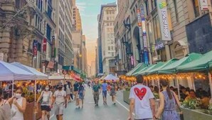 Una strada animata fiancheggiata da edifici, alcuni con insegne visibili, e una folla di persone che cammina.