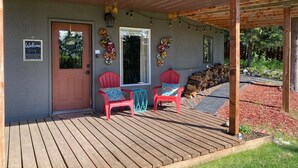 Een houten terras met twee rode stoelen en een blauwgroene stoel, een deur en een welkomstbord.