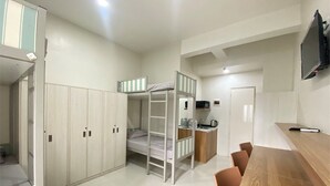 A compact room with bunk beds, a kitchenette, a TV, and a wooden table.