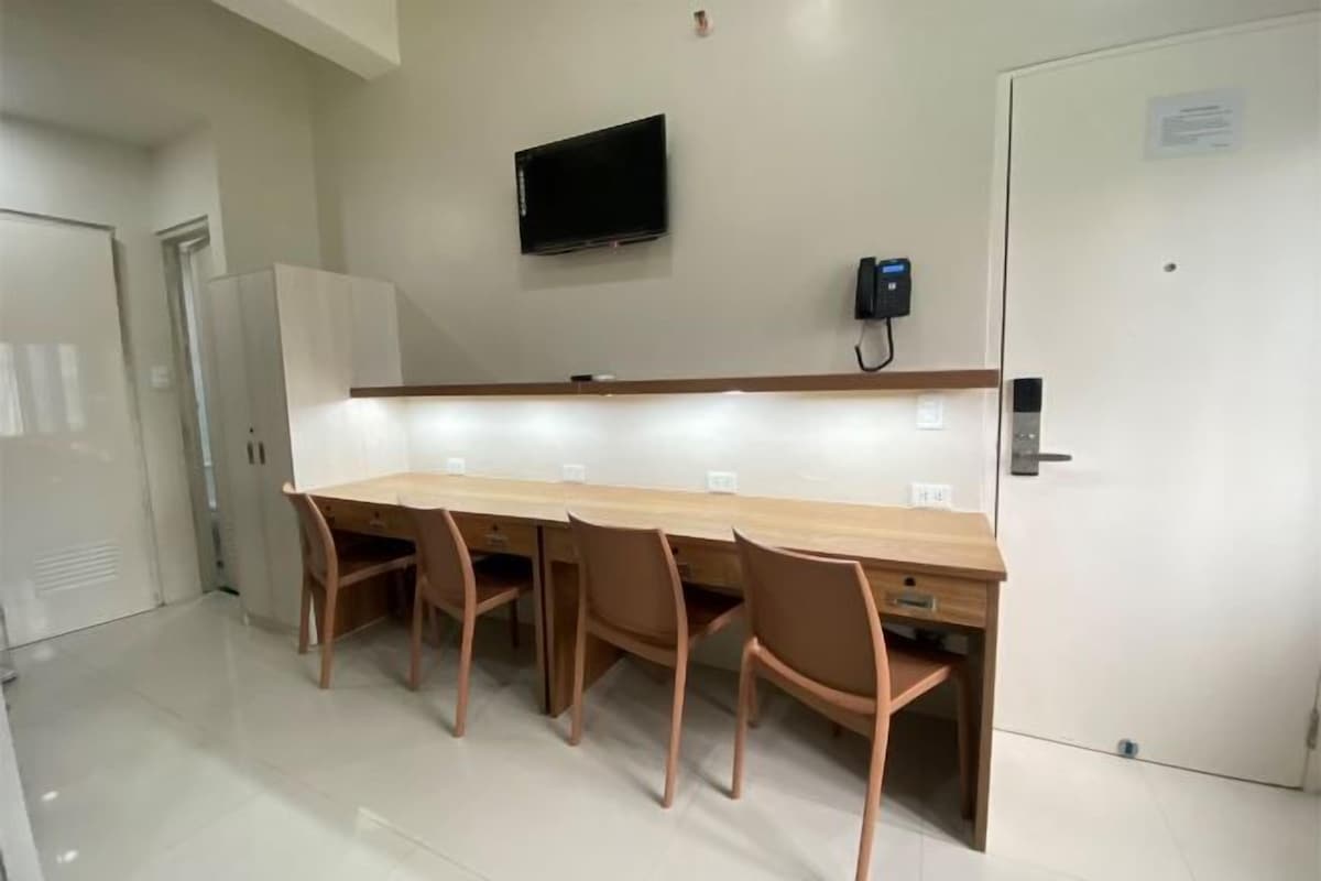 A conference room with a long table, four chairs, a flat-screen TV, a phone, and a door.