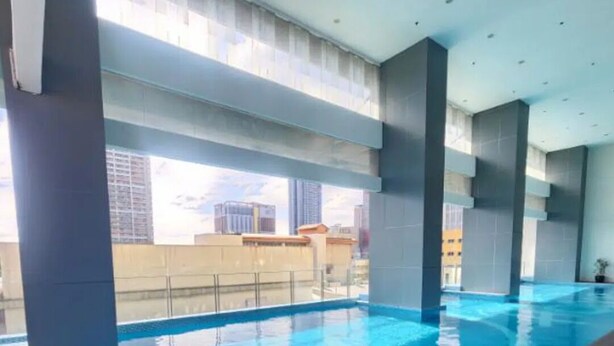 A swimming pool with clear blue water, surrounded by a tiled deck and metal railings.