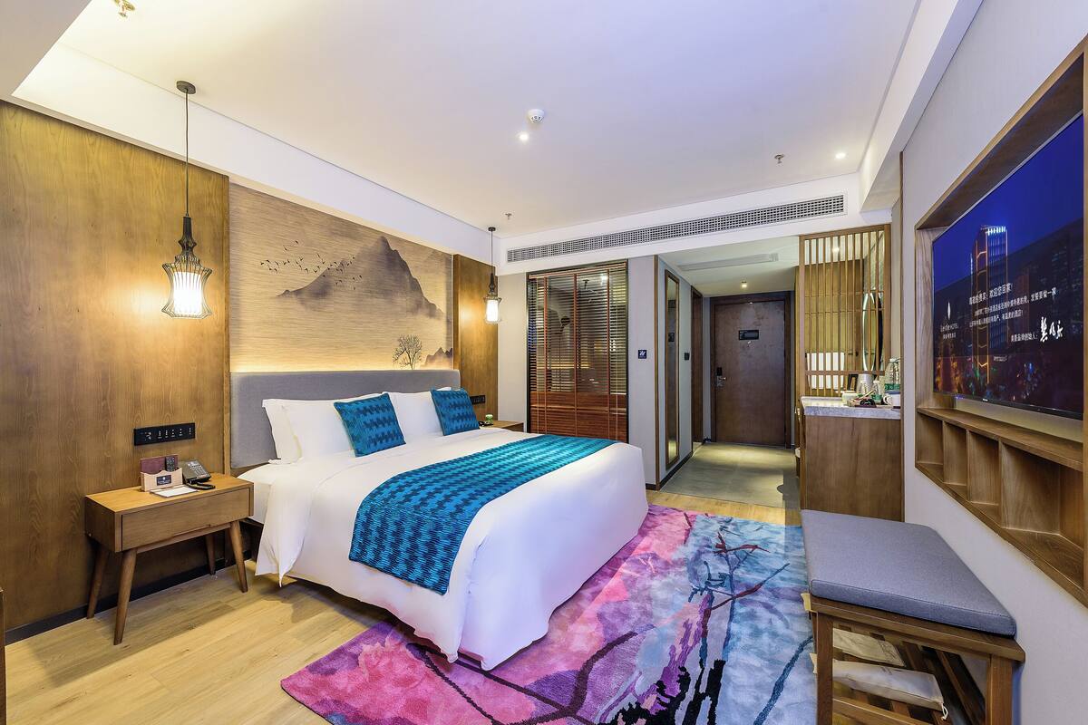 Una habitación de hotel moderna con una cama grande, una mesita de noche y un televisor en la pared.