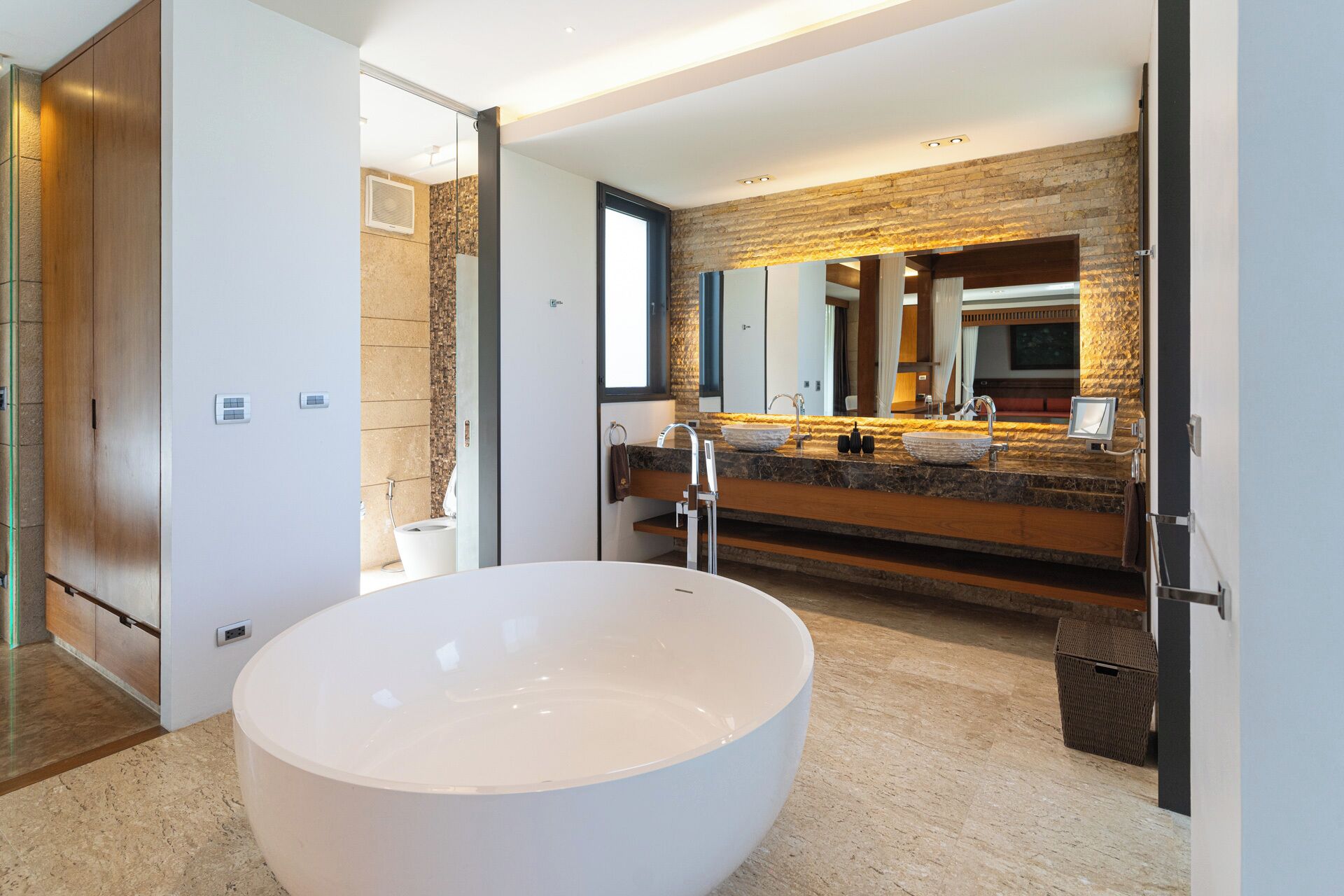 A modern bathroom with a large freestanding bathtub, a double vanity with a stone backsplash, and a large mirror.