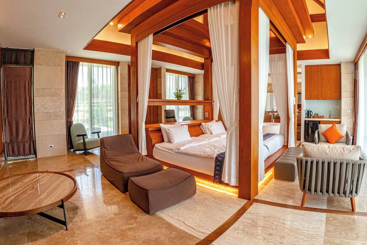A spacious hotel room with a large bed, a sitting area with a chair and ottoman, a small table, and a radiator.
