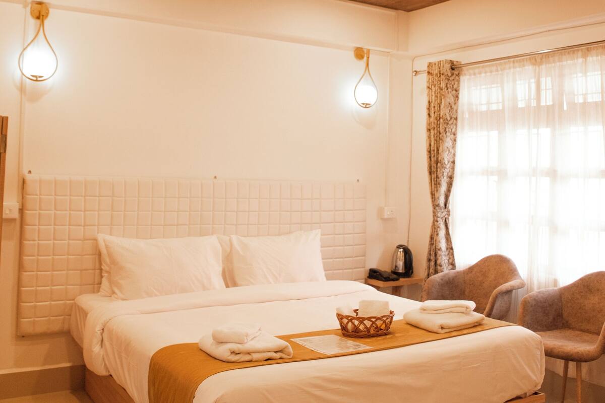 A bedroom with a wooden bed, white bedding, a bedside table, a lamp, and a chair.