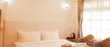 A bedroom with a wooden bed, white bedding, a bedside table, a lamp, and a chair.