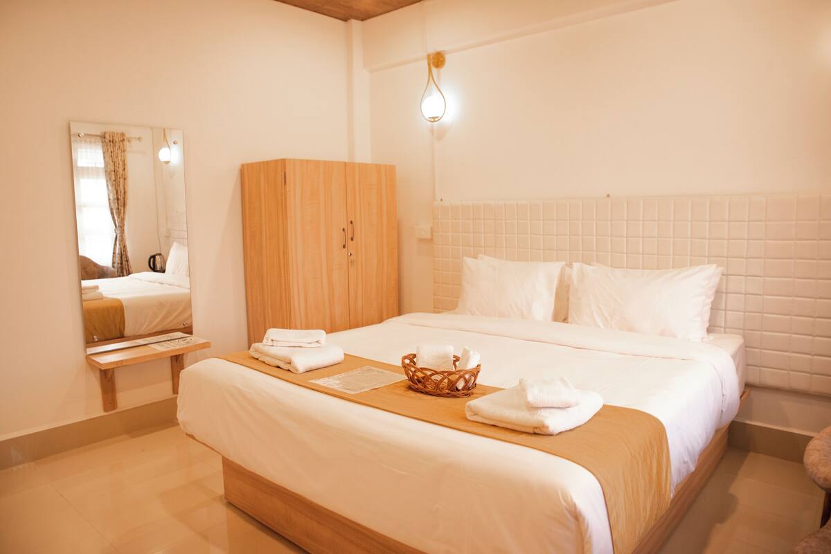 A hotel room with a large bed, a wooden wardrobe, a bedside table, and a mirror.