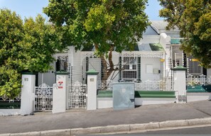 Un edificio residencial con puerta de acceso, techo verde, paredes blancas y portón metálico.