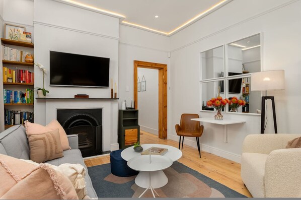 Una sala de estar moderna con chimenea, un televisor de pantalla plana, una estantería y una zona de comedor con mesa y sillas.