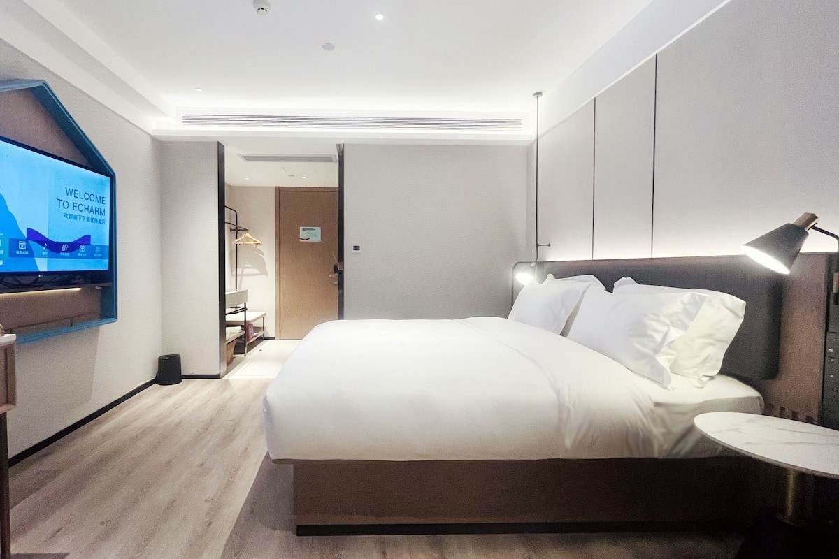 Una moderna camera d'albergo con un letto grande, una scrivania con televisore a schermo piatto e un comodino con lampada.