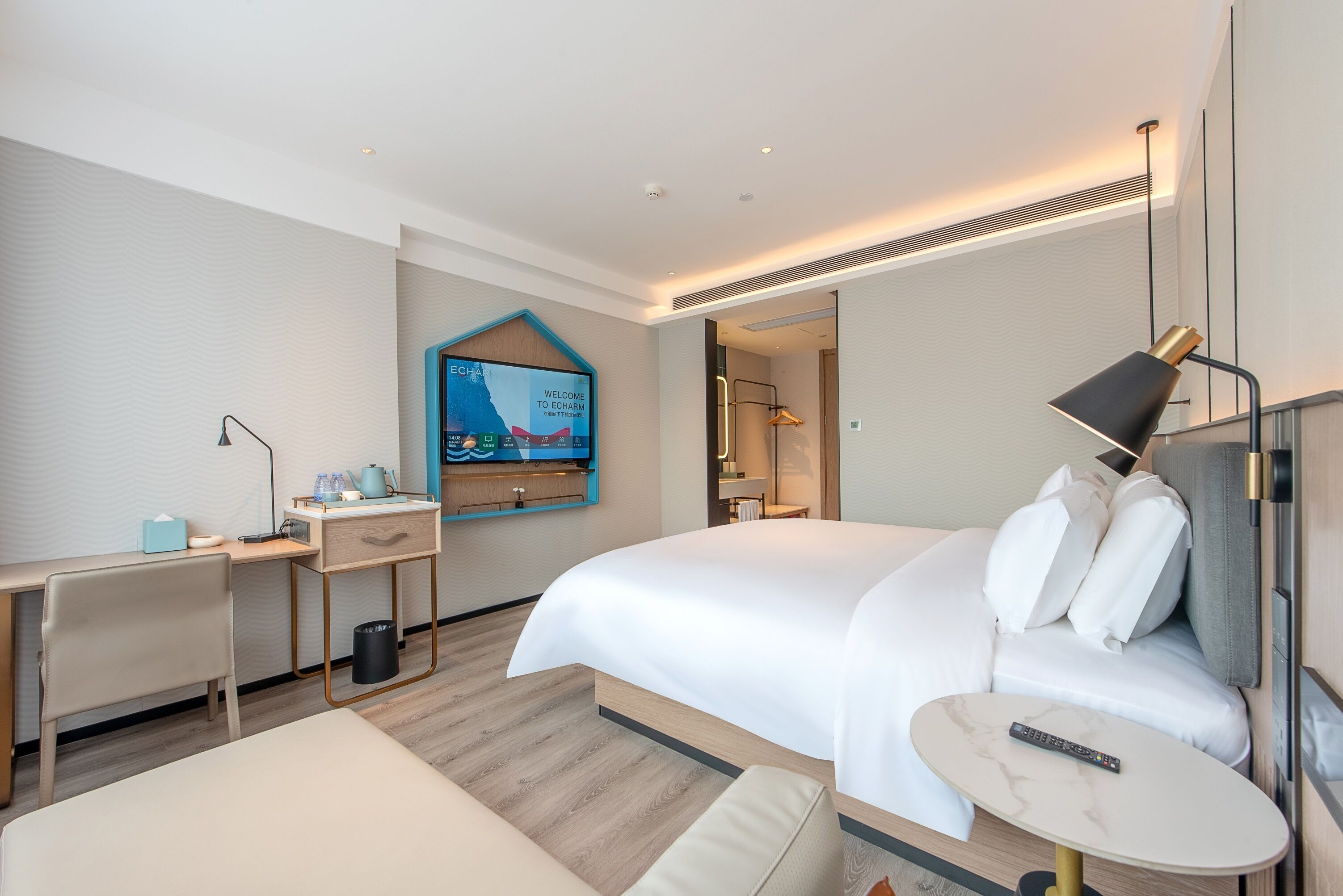 A modern hotel room with a large bed, a desk, a chair, and a small table.