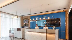 A hotel reception area with a marble reception desk, a blue wall with a coffee menu, and a glass display case. - Yishang Hotel (Zhanjiang)