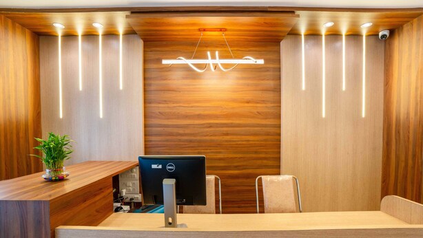 A reception desk with a computer, a potted plant, and a wooden wall with a modern light fixture. - Itsy Hotels Iconic (Pune)