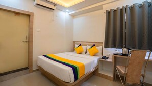 A hotel room with a bed, a desk, a chair, an air conditioning unit, and a curtain. - Itsy Hotels Iconic (Pune)