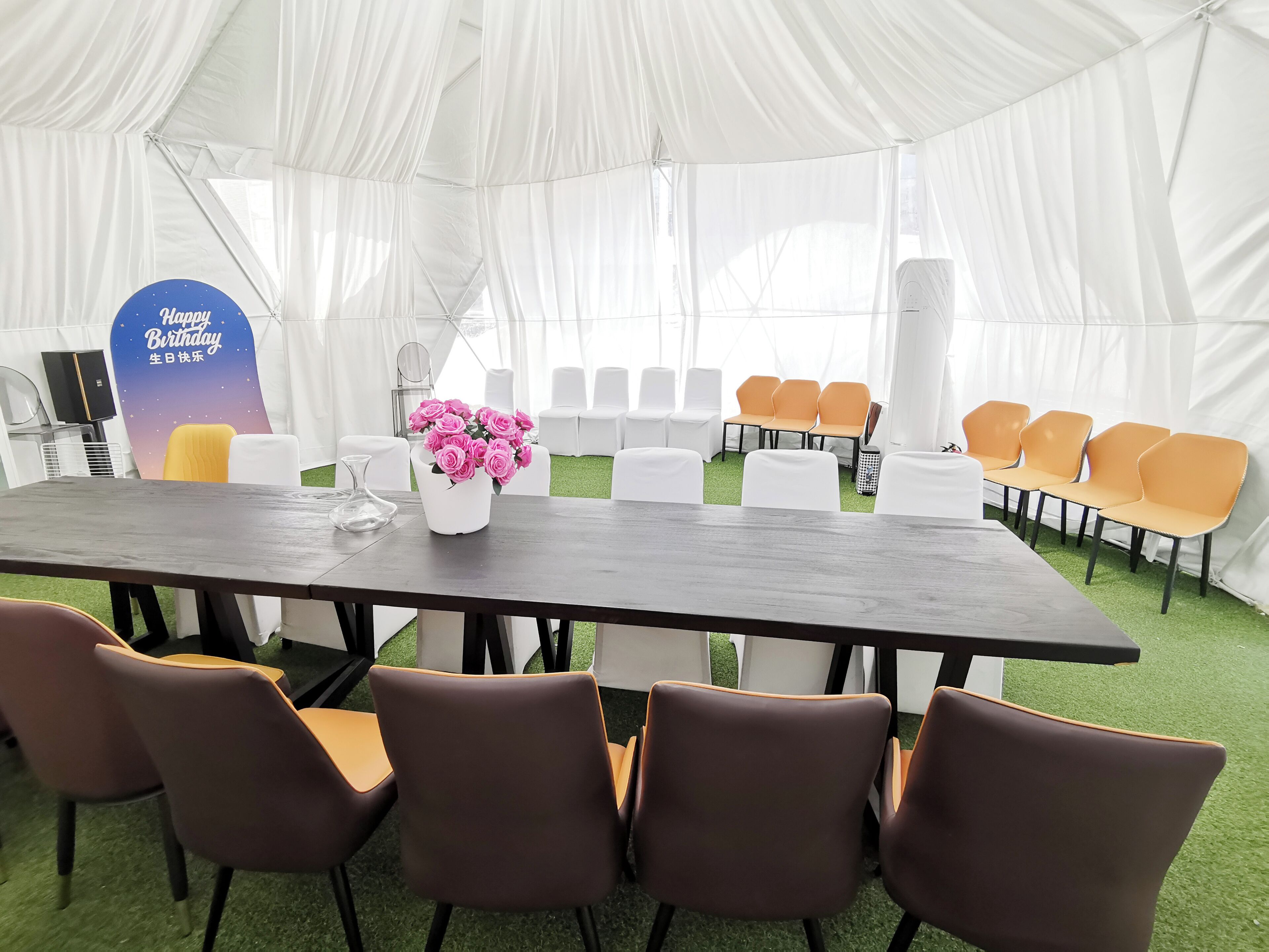 Un espacio para eventos con carpas, una larga mesa, sillas y un cartel que dice 'Feliz Cumpleaños'.
