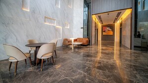 Un vestíbulo moderno con suelo de mármol, una mesa redonda con sillas, un sofá y un pasillo que conduce a otra zona.