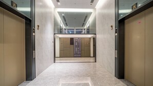A modern elevator area with a marble floor, glass panels, and a digital display.