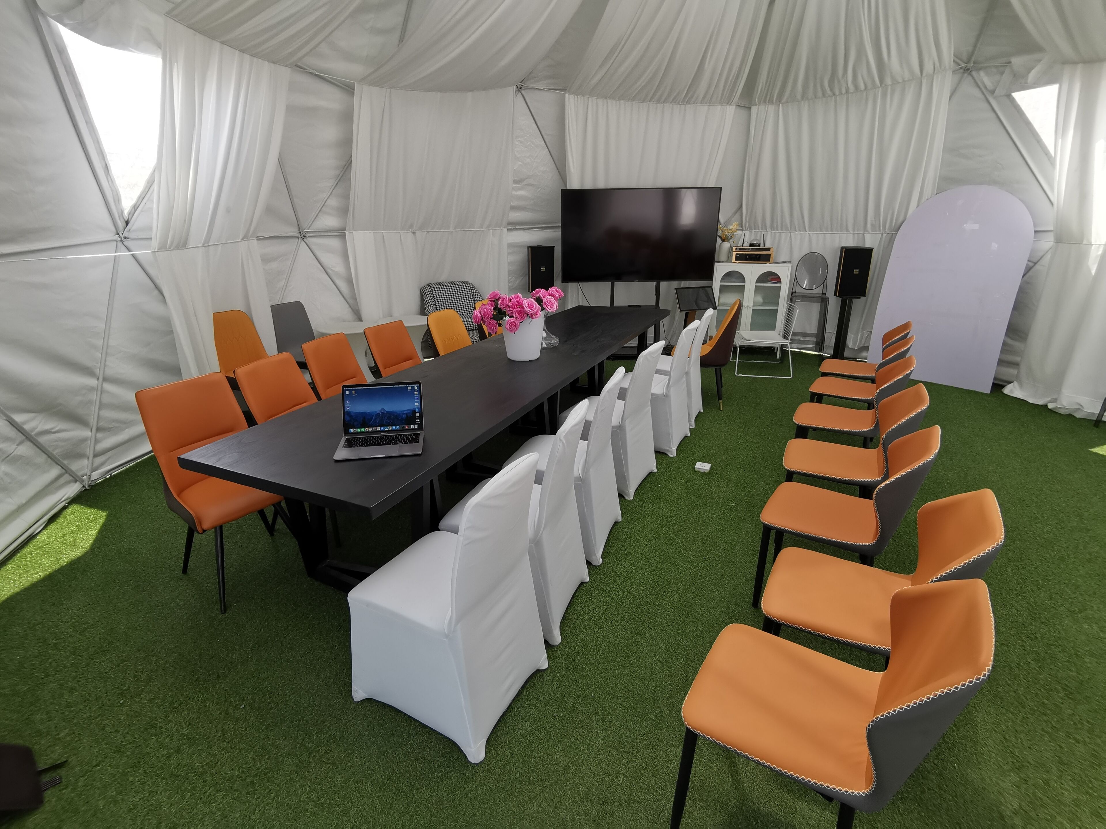Un salón de conferencias con carpas, una mesa larga, sillas, un televisor y un sistema de sonido.