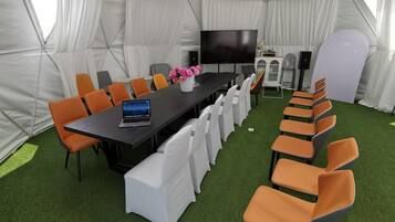 Un salón de conferencias con carpas, una mesa larga, sillas, un televisor y un sistema de sonido.