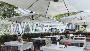 Un área de comedor al aire libre con mesas y sombrillas, rodeada de vegetación.