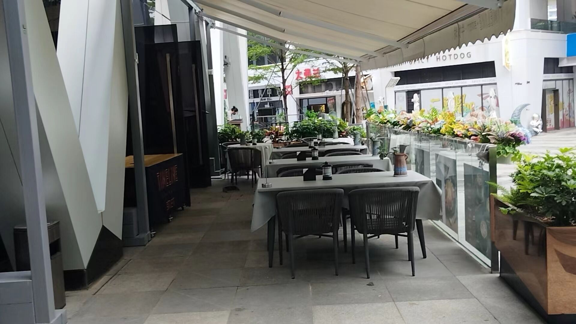 An outdoor dining area with tables and chairs, potted plants, and a view of the street.