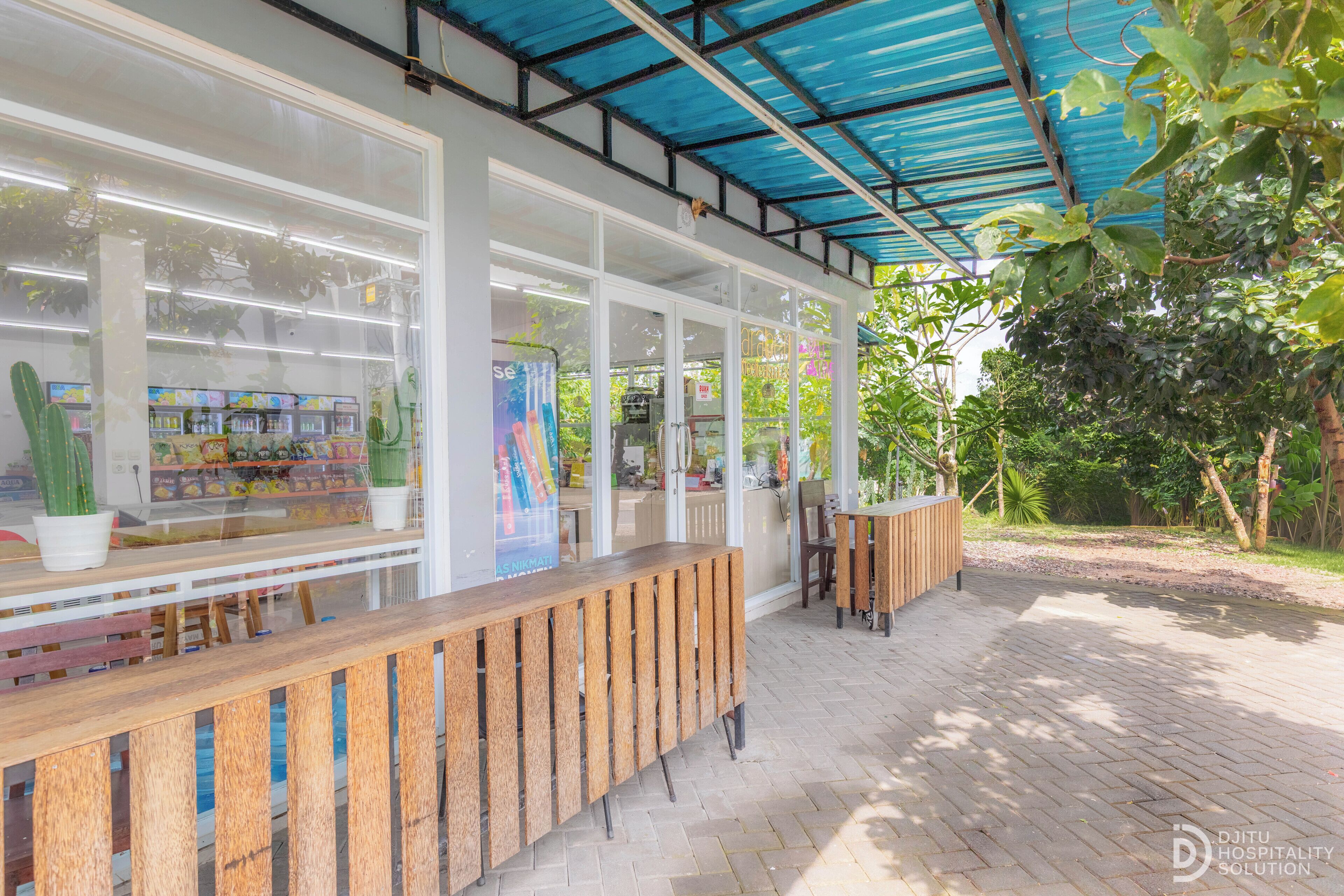 A covered outdoor seating area with a wooden bench, a glass display case with plants, and a view of the surrounding greenery.