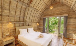 Ein geräumiges Schlafzimmer mit einem großen Bett, Holzbalkendecke und Blick auf Grünfläche.