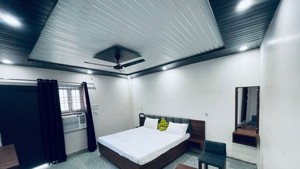 Une chambre à coucher comprenant un lit, un bureau, une chaise, un ventilateur de plafond et une fenêtre avec des rideaux.