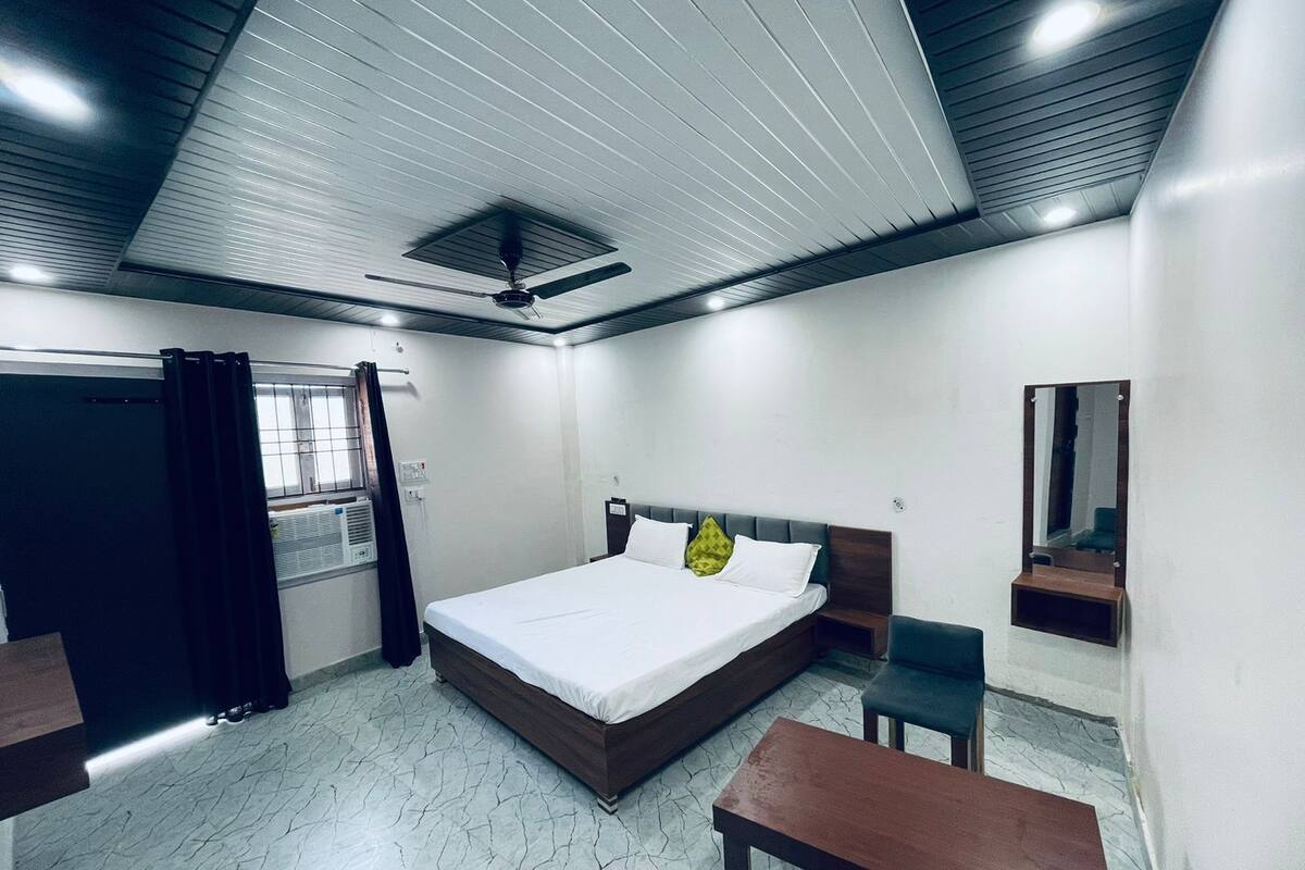 Une chambre à coucher comprenant un lit, un bureau, une chaise, un ventilateur de plafond et une fenêtre avec des rideaux.
