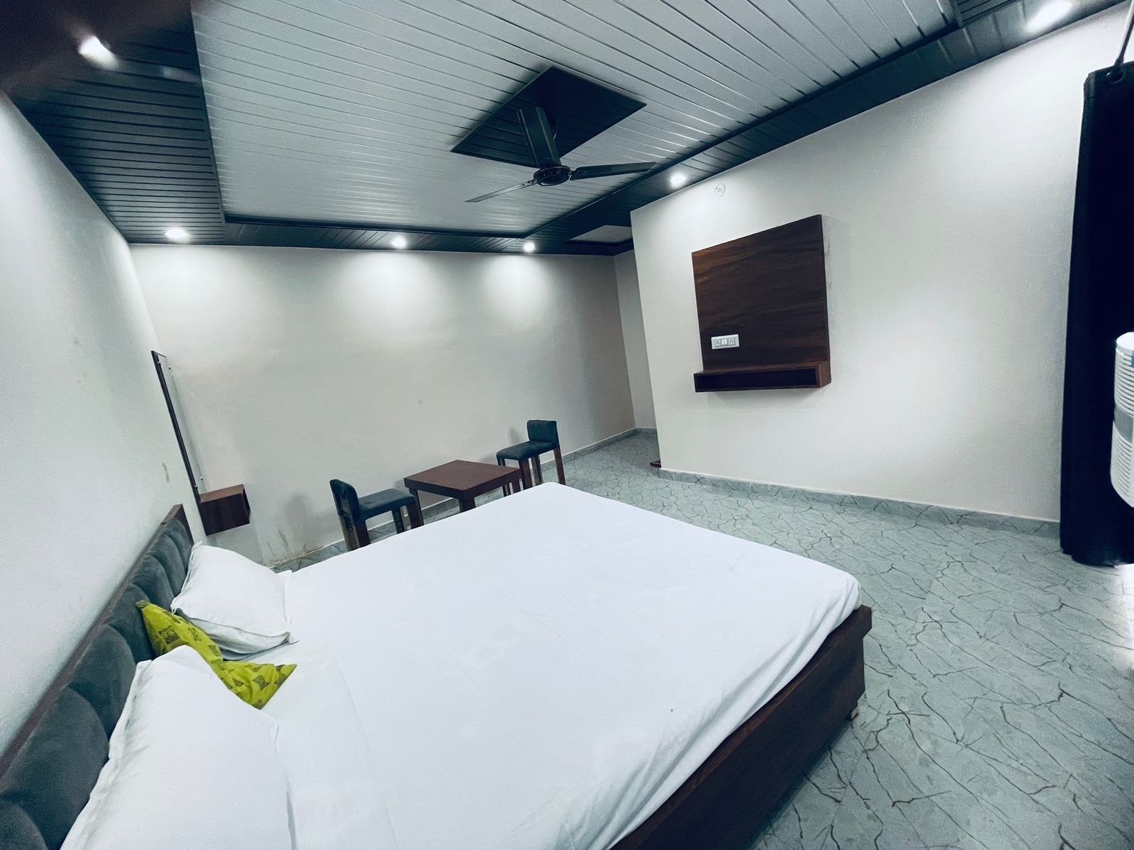 A hotel room with a bed, a desk, a chair, a ceiling fan, and a wall-mounted air conditioner.