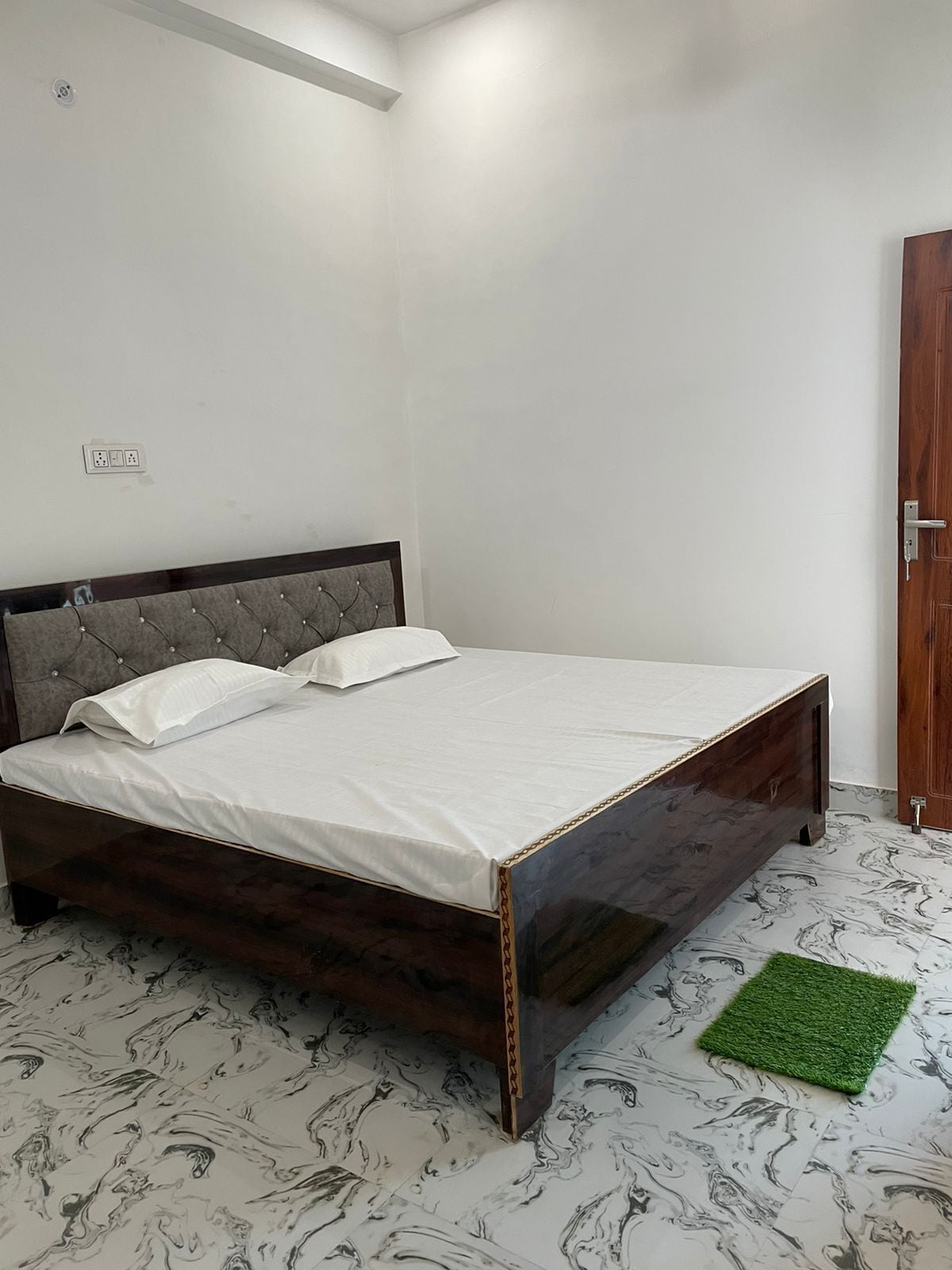 A bedroom with a bed, a power outlet, and a door.