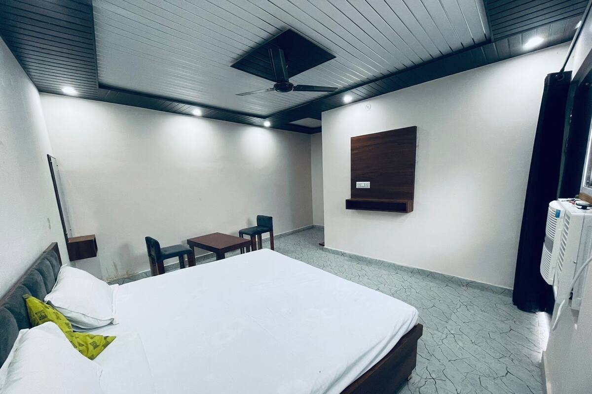 Une chambre d’hôtel équipée d’un lit, d’un bureau, de deux chaises, d’un ventilateur de plafond et d’un radiateur.