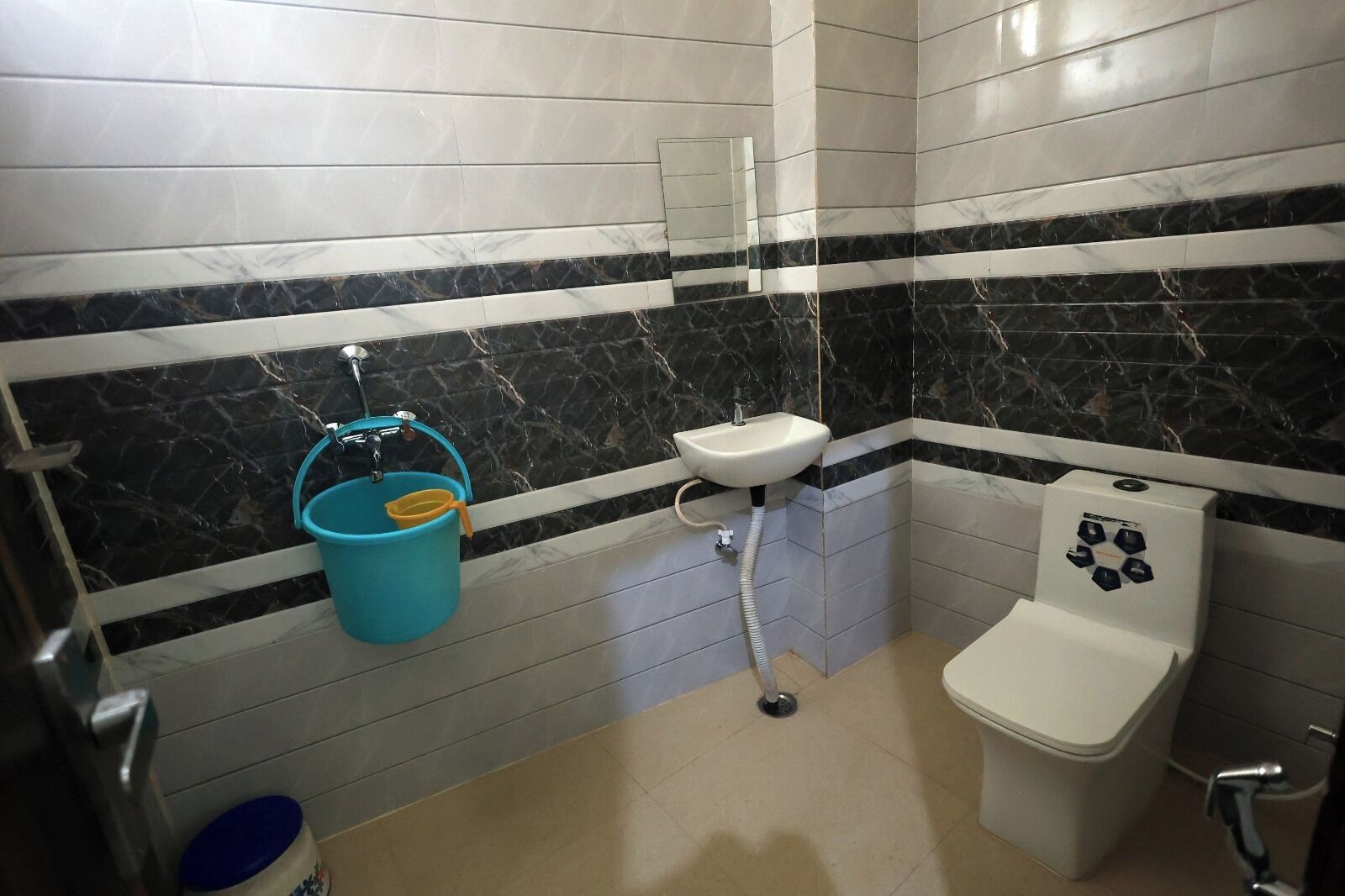 Ein Badezimmer mit Toilette, Waschbecken und einem blauen Eimer.
