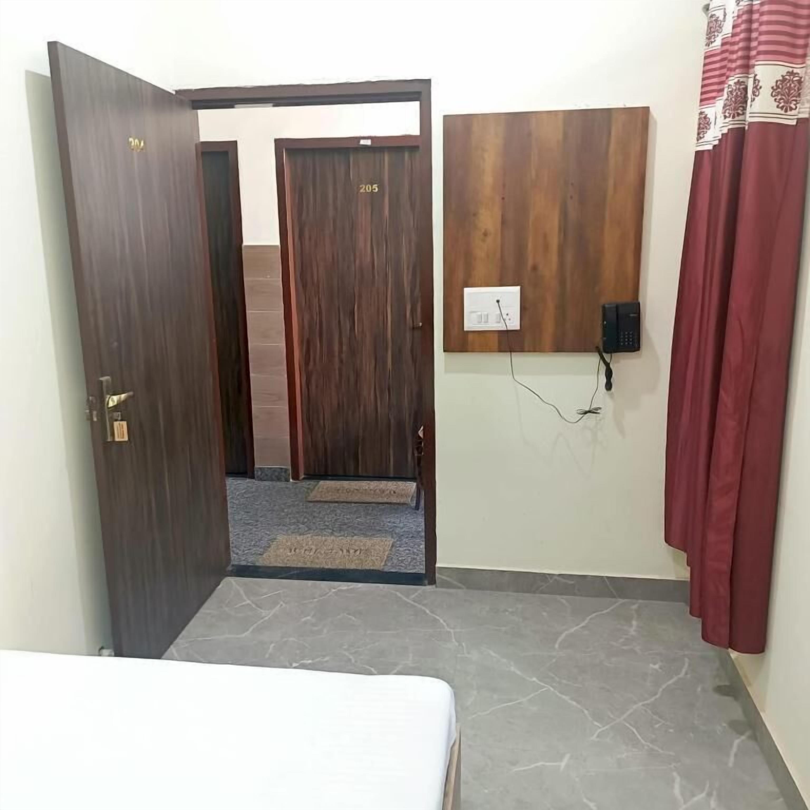 A room with a bed, a wooden door, a wall-mounted phone, and a red curtain.