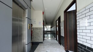 A hallway with a marble floor, a vending machine, and a door with a dark frame. - Shri Girraj Residency (Mathura)