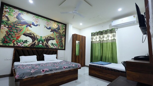 A bedroom with a large bed, a smaller bed, a wardrobe, a ceiling fan, an air conditioning unit, and a television. - Shri Girraj Residency (Mathura)