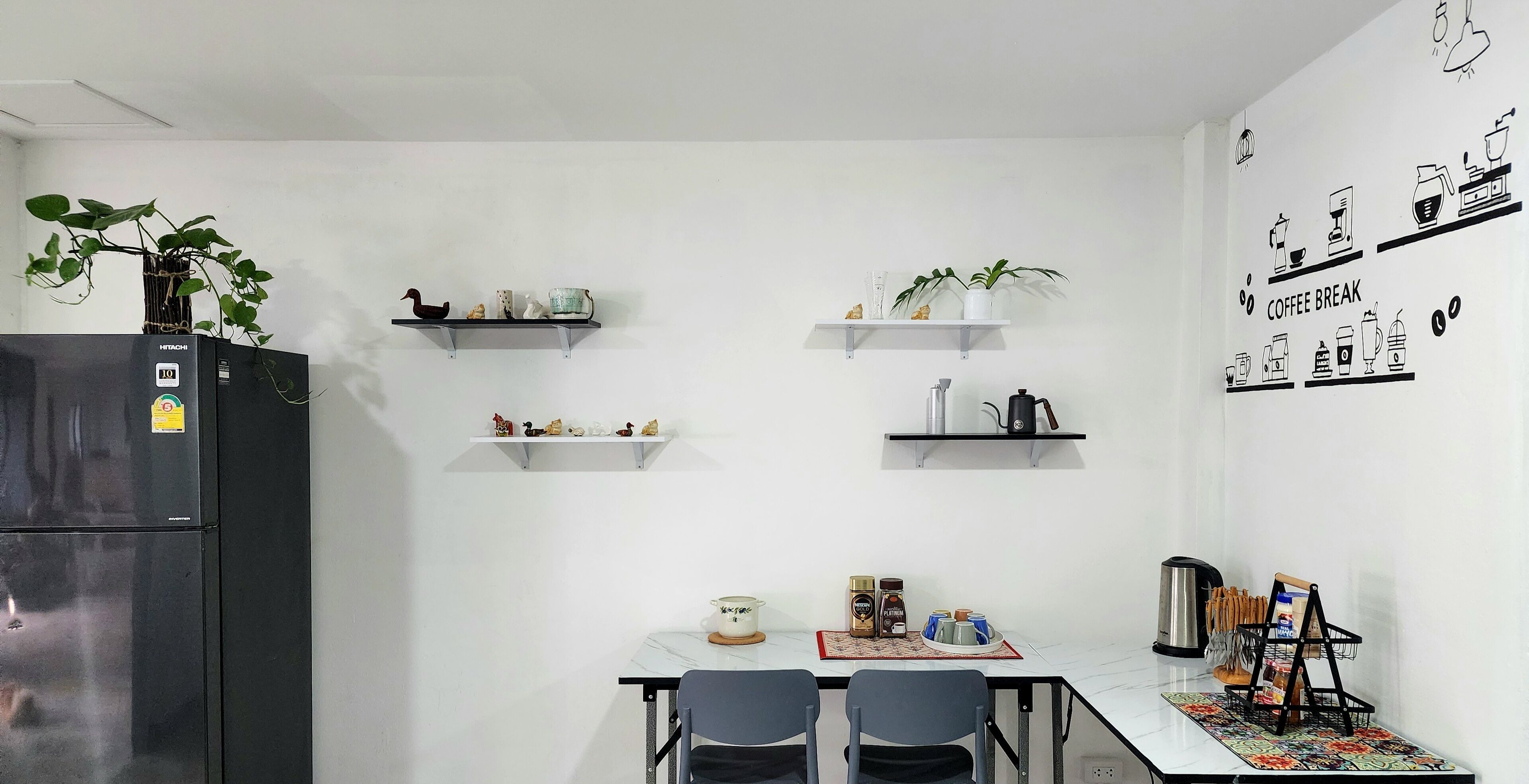 A modern kitchen with white walls, a black refrigerator, and shelves with kitchenware and decorative items.