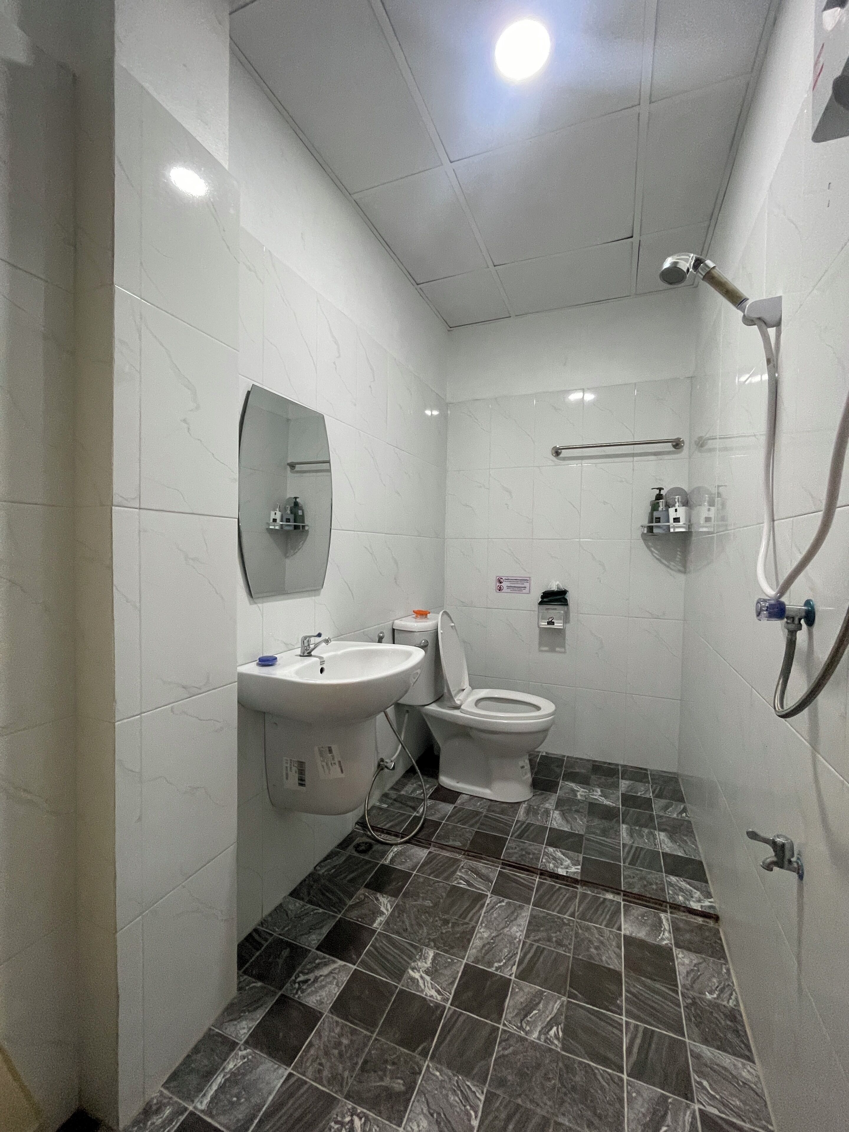 A modern bathroom with white tiles, a sink, a toilet, and a shower area.