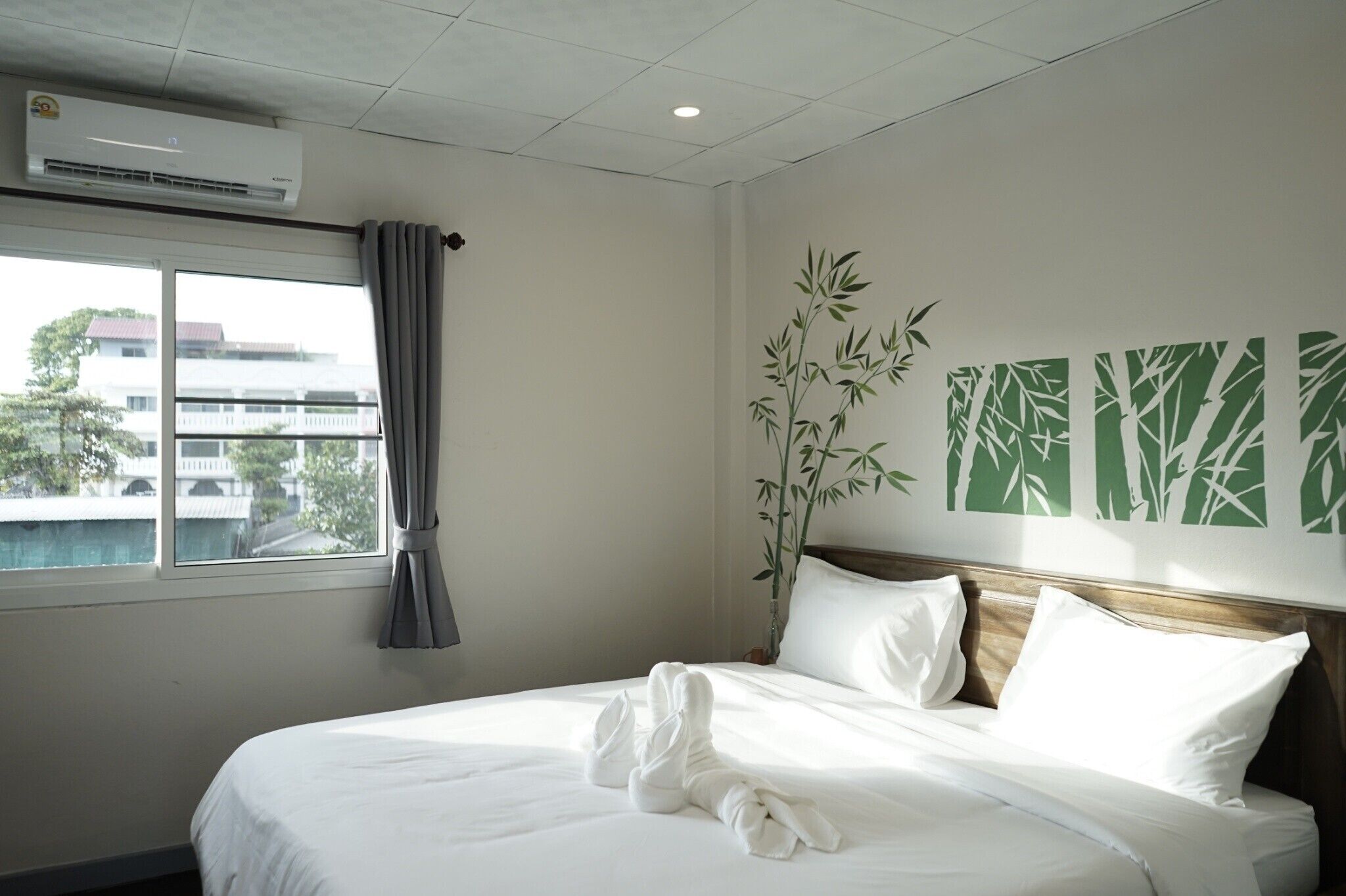 A hotel room with a bed, a window with curtains, an air conditioning unit, and a wall with bamboo artwork.